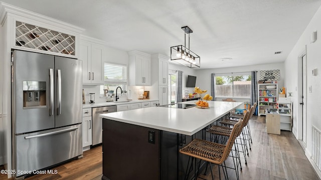 kitchen featuring a kitchen island with sink, appliances with stainless steel finishes, light countertops, white cabinets, and dark wood-style floors