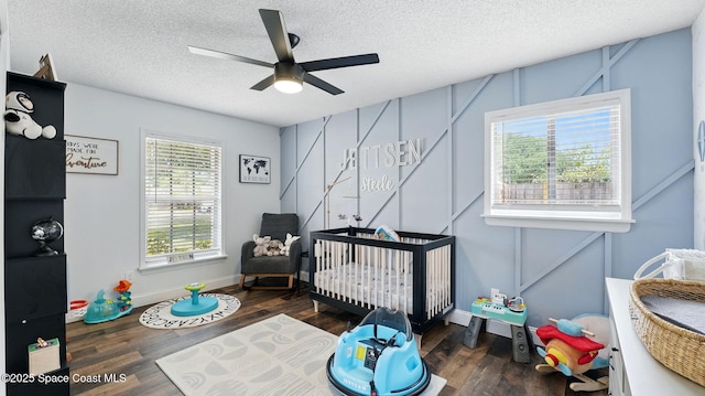bedroom featuring wood finished floors, baseboards, a textured ceiling, and a nursery area
