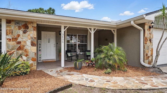 view of exterior entry with a garage, stucco siding, a porch, and stone siding