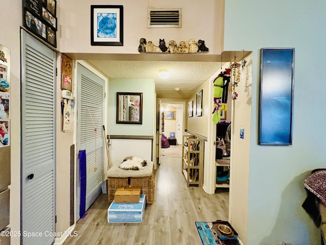 hallway with visible vents, a textured ceiling, and light wood-type flooring