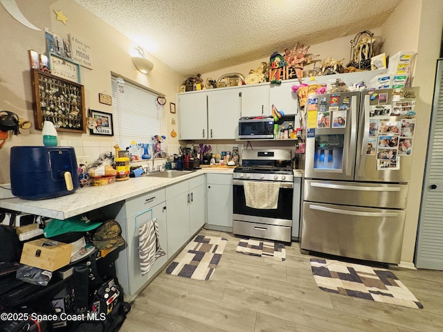 kitchen featuring light wood-style floors, light countertops, a textured ceiling, a sink, and appliances with stainless steel finishes
