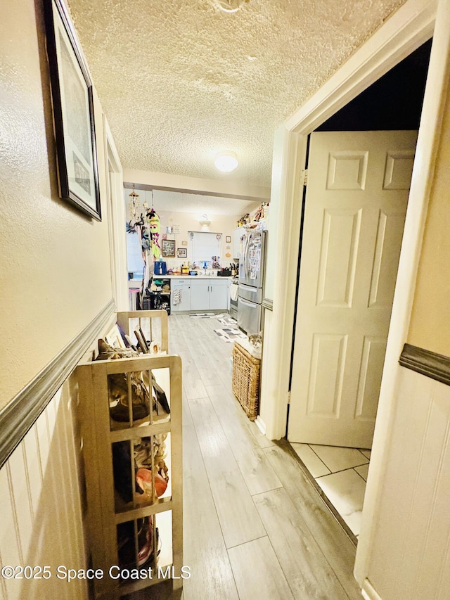 hallway with a textured ceiling and light wood-style flooring