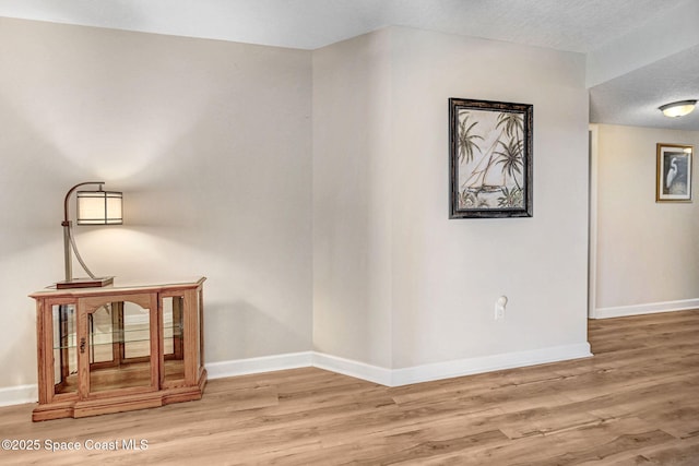 corridor with a textured ceiling, baseboards, and wood finished floors