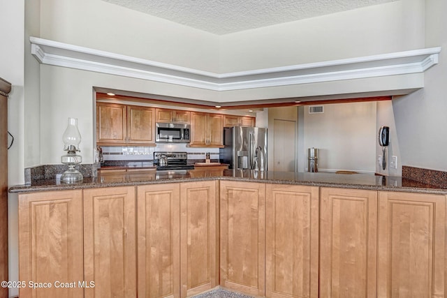 kitchen featuring a textured ceiling, visible vents, appliances with stainless steel finishes, a peninsula, and dark stone counters