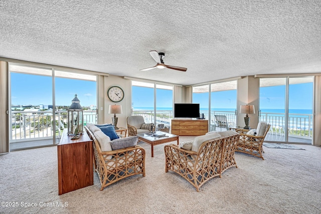 living room featuring carpet floors, a ceiling fan, a textured ceiling, and a wall of windows
