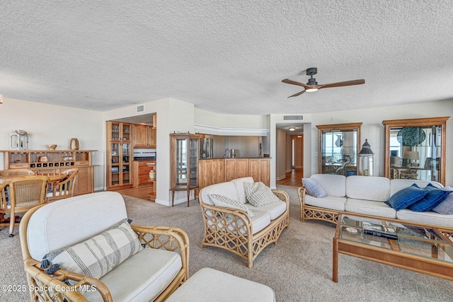 living room with visible vents, a textured ceiling, ceiling fan, and light carpet