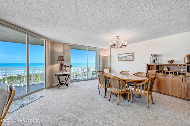 dining area featuring an inviting chandelier, a water view, expansive windows, and light colored carpet