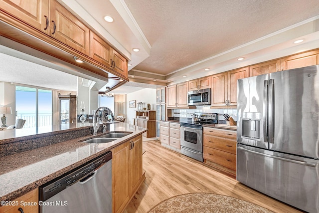 kitchen with dark stone counters, a textured ceiling, a sink, light wood-style flooring, and appliances with stainless steel finishes