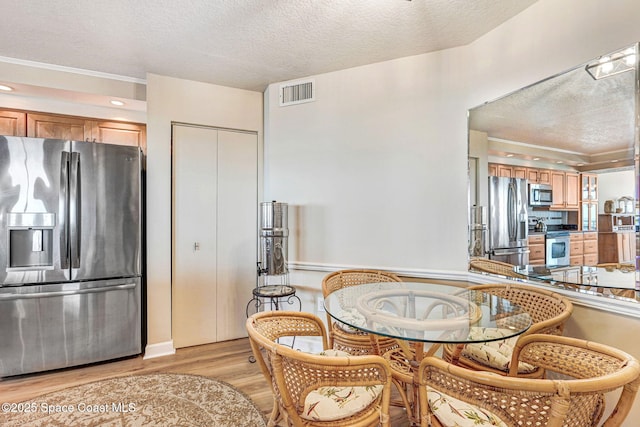 dining space with light wood-type flooring, a textured ceiling, and visible vents