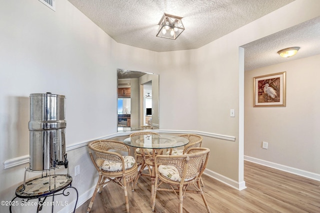 dining area featuring baseboards, a textured ceiling, wood finished floors, and visible vents