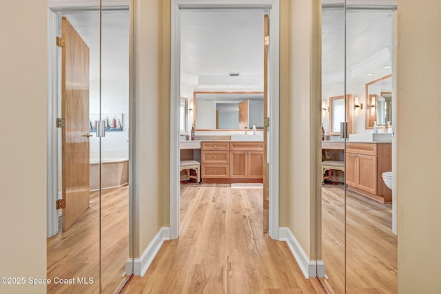 hall with baseboards, a sink, and light wood-style floors