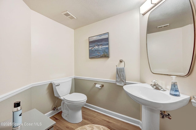 half bath featuring baseboards, toilet, wood finished floors, and visible vents