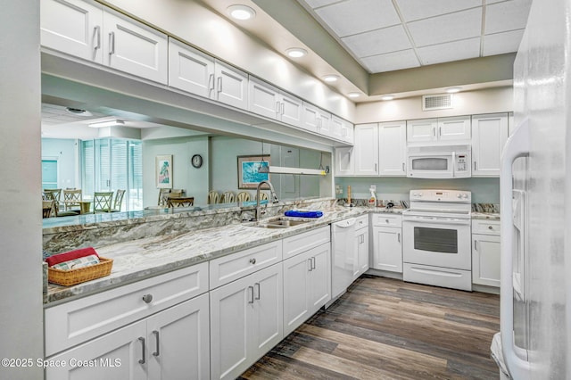 kitchen featuring white cabinets, light stone countertops, a sink, white appliances, and visible vents