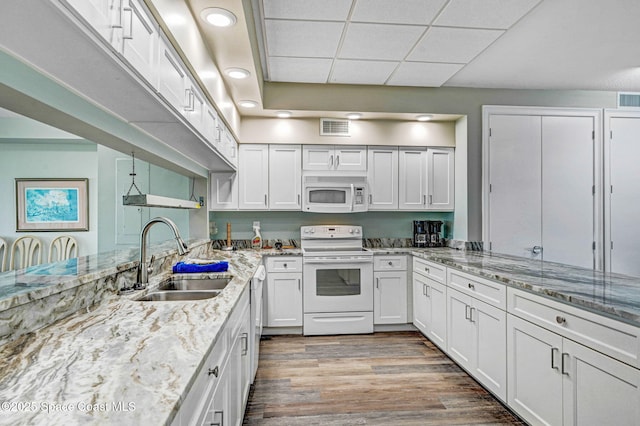 kitchen with a sink, white appliances, white cabinetry, and visible vents
