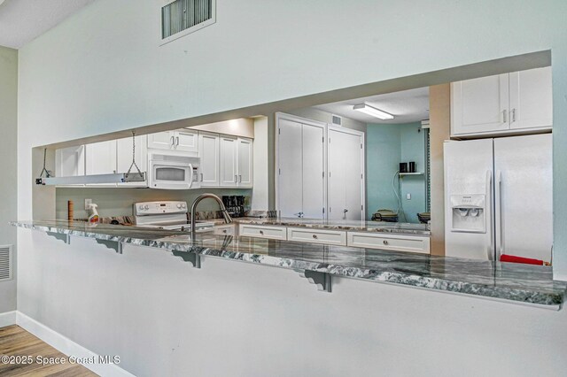 kitchen with visible vents, dark stone counters, a peninsula, and white appliances