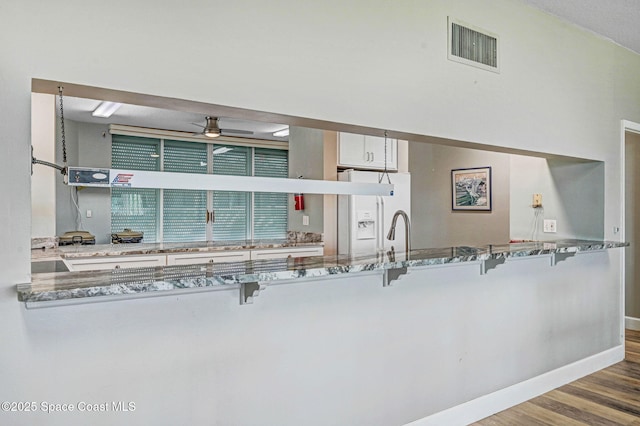 kitchen with visible vents, stone countertops, baseboards, ceiling fan, and a kitchen bar