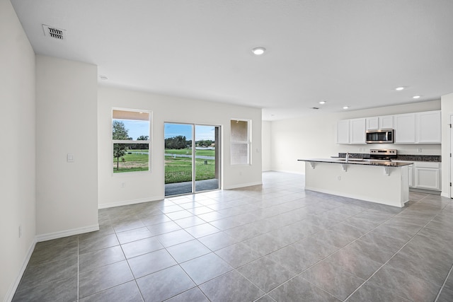 unfurnished living room featuring visible vents, baseboards, recessed lighting, a sink, and light tile patterned floors