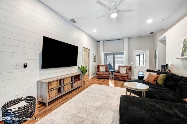 living area with visible vents, wood walls, ceiling fan, and wood finished floors
