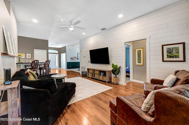 living room featuring wood walls, a ceiling fan, recessed lighting, wood finished floors, and visible vents