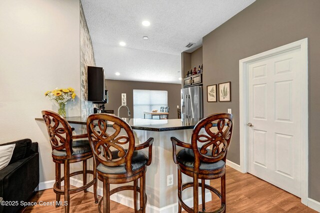 kitchen with a textured ceiling, a breakfast bar, stainless steel fridge, and light wood-style flooring