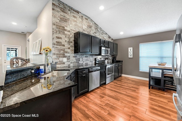 kitchen featuring backsplash, appliances with stainless steel finishes, light wood-type flooring, a sink, and lofted ceiling
