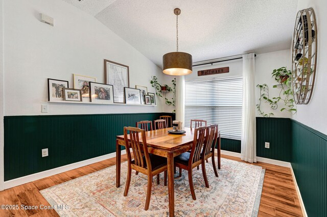 dining room featuring a textured ceiling, wood finished floors, lofted ceiling, and a wainscoted wall