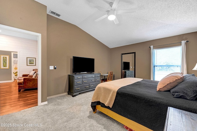 bedroom featuring a ceiling fan, a textured ceiling, visible vents, lofted ceiling, and light carpet
