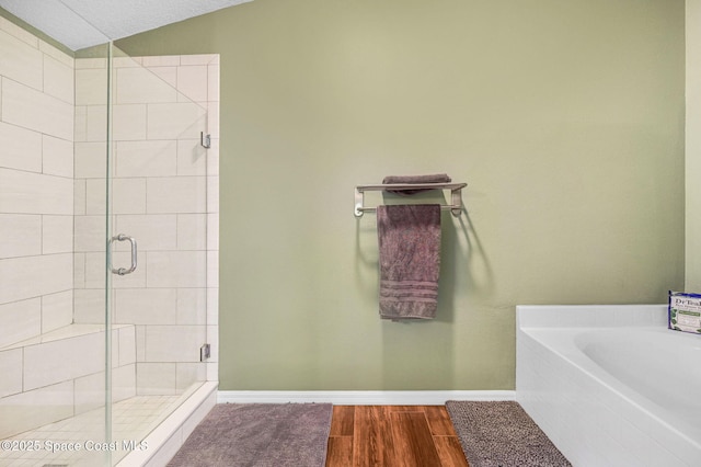 full bathroom featuring a garden tub, a stall shower, wood finished floors, baseboards, and lofted ceiling