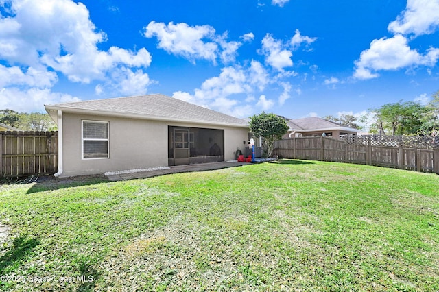 rear view of house featuring a yard, a fenced backyard, a sunroom, and stucco siding