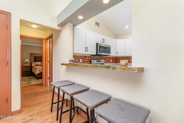 1435 Xavier Ave SE, Palm Bay, FL 32909 - kitchen with visible vents, a kitchen breakfast bar, stainless steel microwave, white cabinets, and light wood finished floors