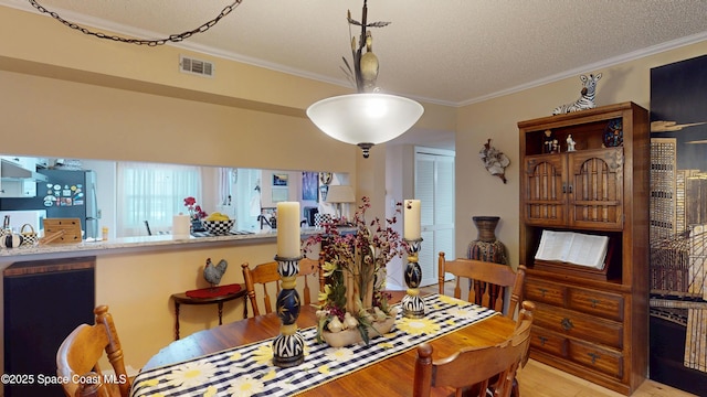 dining room with crown molding, a textured ceiling, and light wood finished floors
