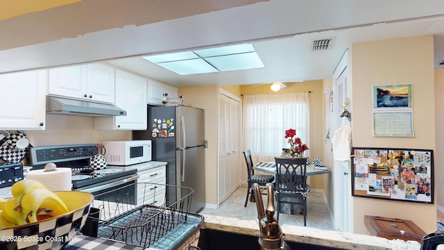 kitchen with under cabinet range hood, range with electric cooktop, white microwave, white cabinets, and freestanding refrigerator