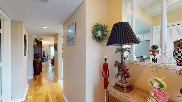 hallway with a textured ceiling, ornate columns, light wood-style floors, baseboards, and recessed lighting