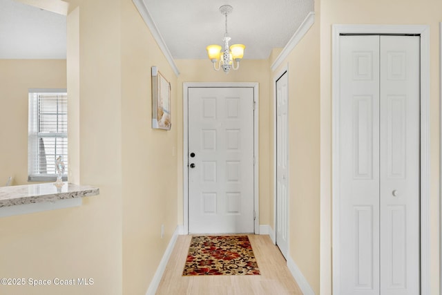 doorway to outside with baseboards, a notable chandelier, light wood finished floors, and a textured ceiling