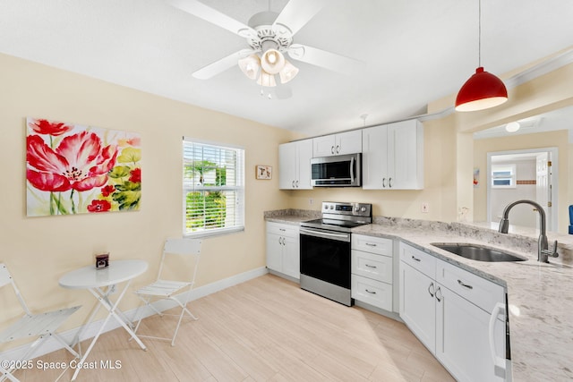 kitchen with white cabinets, appliances with stainless steel finishes, light stone countertops, and a sink