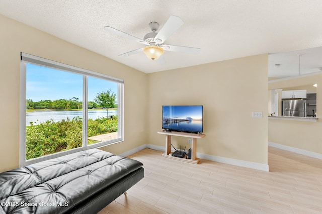 living room with ceiling fan, baseboards, and light wood-type flooring