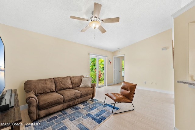 living area featuring baseboards, lofted ceiling, ceiling fan, and a textured ceiling