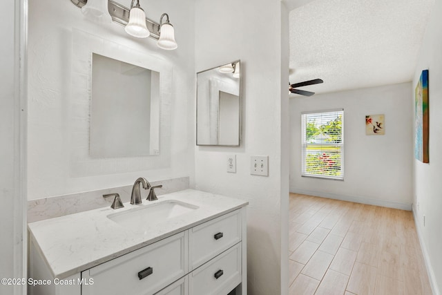 bathroom with a textured ceiling, baseboards, vanity, and ceiling fan