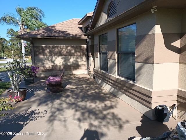 view of side of property with a patio, roof with shingles, and stucco siding