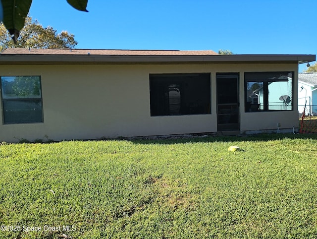 rear view of property with a lawn, a sunroom, and stucco siding