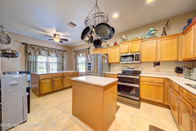 kitchen featuring light tile patterned flooring, a kitchen island, ceiling fan, light countertops, and appliances with stainless steel finishes