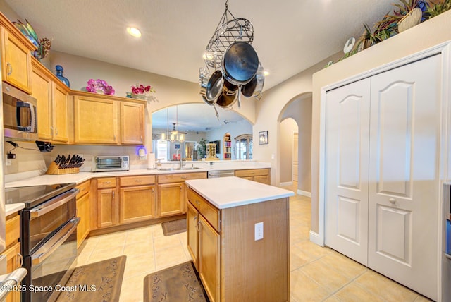 kitchen with appliances with stainless steel finishes, light countertops, arched walkways, a center island, and recessed lighting