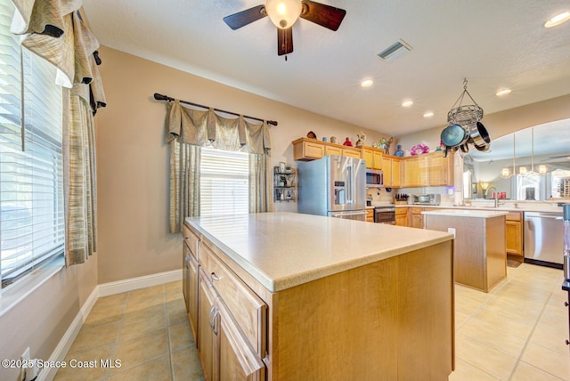 kitchen featuring ceiling fan, a kitchen island, light brown cabinets, and stainless steel appliances
