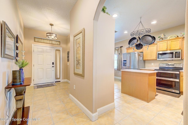 interior space featuring appliances with stainless steel finishes, light brown cabinets, light countertops, arched walkways, and a center island