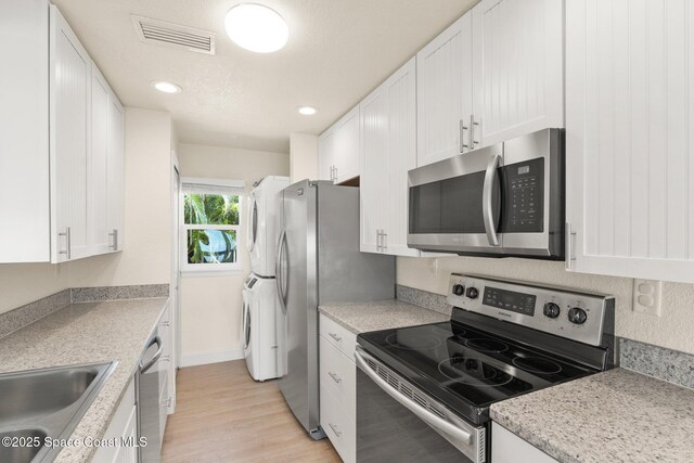 1495 Newfound Harbor Dr, Merritt Island, FL 32952 - kitchen featuring appliances with stainless steel finishes, a sink, white cabinetry, visible vents, and stacked washer and clothes dryer