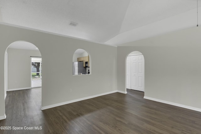 spare room with visible vents, baseboards, dark wood-type flooring, arched walkways, and vaulted ceiling