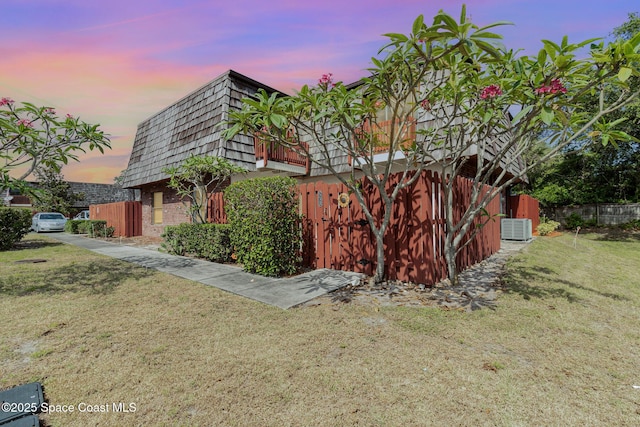 53 Piney Branch Way Unit D, West Melbourne, FL 32904 - property exterior at dusk featuring a lawn, brick siding, mansard roof, fence, and central AC