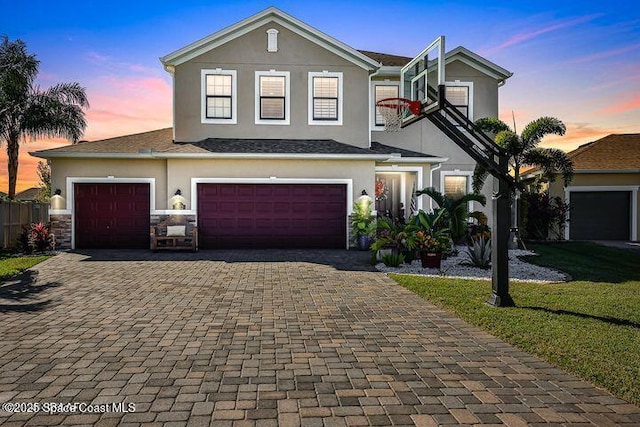 traditional home featuring decorative driveway, stucco siding, a yard, and stone siding