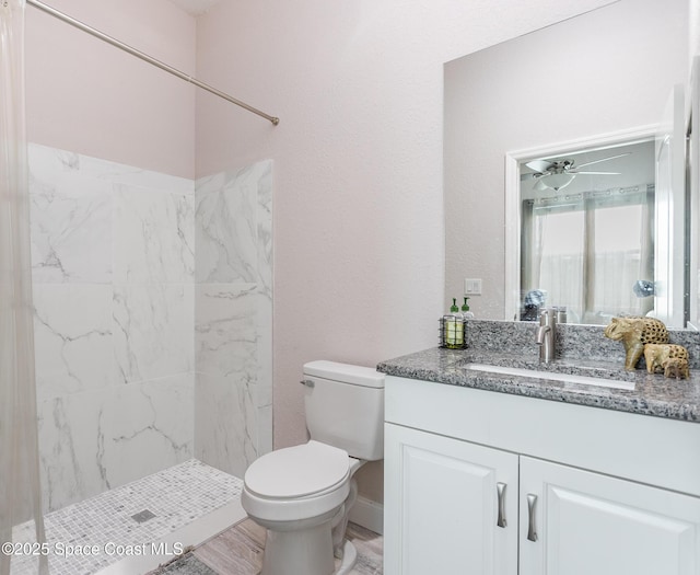 full bath with a tile shower, vanity, toilet, a ceiling fan, and baseboards