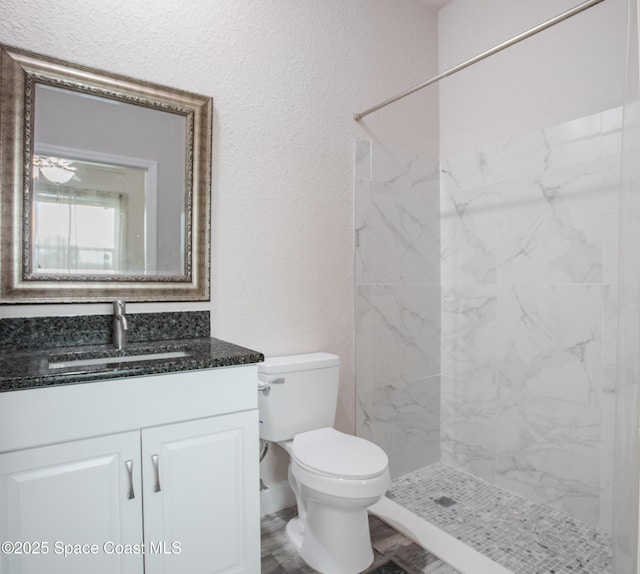 full bathroom with a textured wall, vanity, toilet, a marble finish shower, and wood finished floors